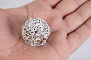 Gesundes Essen: Energiekugel mit Datteln und Kokosraspeln in der Hand