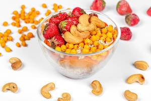Gesundes Frühstück in einer Glasschüssel mit Haferflocken, Erdbeeren, Cashew Nüssen und Sanddornbeeren auf weißem Hintergrund