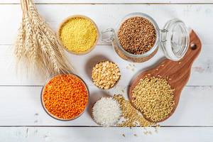 Getreide wie Reis, Weizen, Hirse, Linsen, Erbsen und Buchweizen mit Ähren auf weißem Holztisch