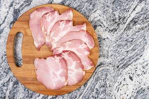 Getrocknetes Schweinefleisch in Scheiben geschnitten auf rundem Holzteller und marmorierter Oberfläche