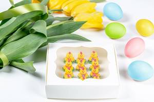 Gift box with a sweet dessert in the shape of chickens, colorful eggs and yellow tulips