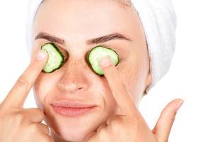Girl holds fingers slices of cucumber in front of her eyes