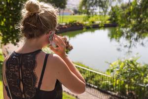 Girl in a black lace dress talking on the phone in a city park on a sunny day