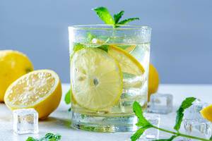 Glas mit erfrischender Limonade mit Zitronenscheibe und Minzeblättern umgeben von Zutaten