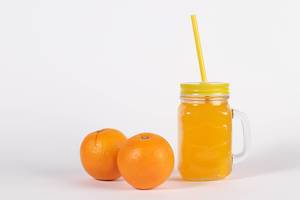 Glas mit Schraubdeckel und Strohhalm gefüllt mit frisch gepresstem Orangensaft neben zwei Orangen