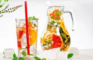 Glass and jug with a cold summer drink of mint, orange, grapefruit and lemon