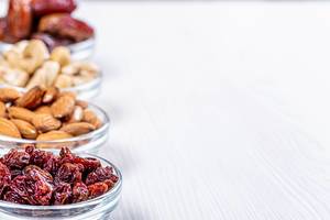 Glass bowls with nuts and dried fruits on white wooden background with free space