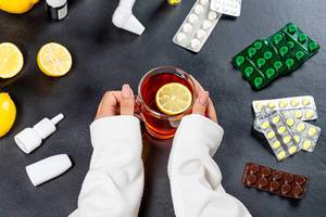 Glass Cup of tea with a piece of lemon in the hands of women surrounded by pills and medicines (Flip 2019)