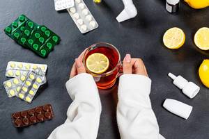 Glass Cup of tea with a piece of lemon in the hands of women surrounded by pills and medicines