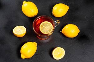Glass Cup with black tea surrounded by fresh ripe lemons on a black background