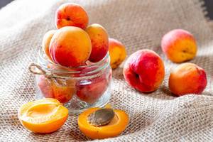 Glass jar with apricots on burlap background
