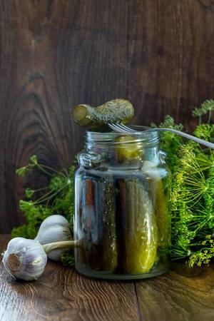 Glass jar with pickles, dill and garlic on wooden background