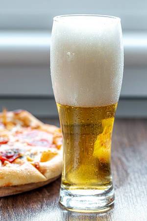 Glass of beer with foam and pizza on the table