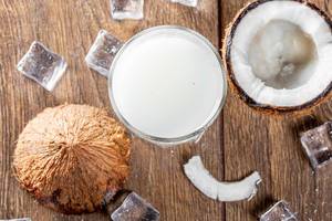 Glass of coconut milk with fresh coconut and ice on a brown wooden background