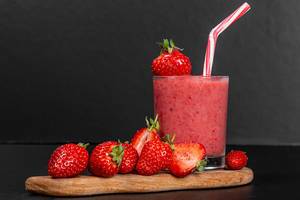 Glass of strawberry smoothie with fresh strawberries on a black background