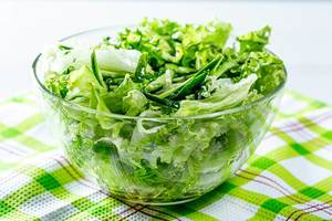Glasschale mit grünem Salat aus Blattsalat, Gurke und Kräutern auf grün-weißem Tuch