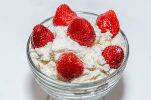 Glasschale mit Hüttenkäse, dekoriert mit frischen ganzen Erdbeeren vor weißem Hintergrund