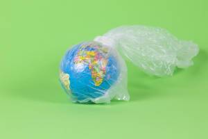 Globe in a plastic bag on green background - Concept on the worldwide plastic problem