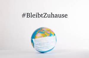 Globe with medical mask and #BleibtZuhause text on white background