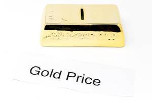 Goldbarren und Papier mit den Worten GOLD PRICE vor weißem Hintergrund