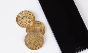 Golden coins next to smartphone on white background