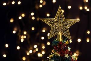 Golden star on top of a decorated Christmas tree on bokeh background