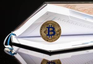Goldene Bitcoin-Münze in einem offenen Notizbuch vor schwarzem Hintergrund