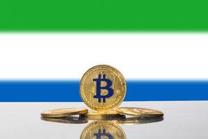Goldene Bitcoins drapiert vor der Flagge des westafrikanischen Staates Sierra Leone