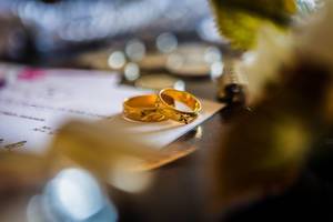 Goldene, verzierte Eheringe liegen auf Hochzeitseinladung - fotografiert mit Bokeh Vordergrund