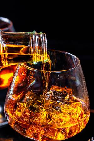 Goldener Cognac wird in mit Glas mit Eiswürfeln eingegossen