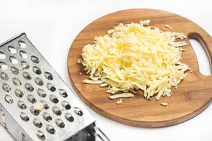 Grated yellow cheese on the wooden board with metal grater