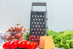 Grater with cheese and fresh vegetables on the kitchen table