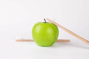 Green apple with wooden toothbrushes on white background (Flip 2019)