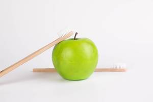 Green apple with wooden toothbrushes on white background