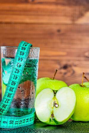 Green apples and a glass of water with measuring tape on wooden background. Diet concept