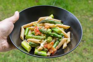 Green asparagus with penne pasta, tomato and mozzarella. Holding plate in hand