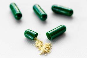 Green whole capsules and one open with powder poured out of it on a white background