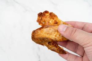 Grilled Chicken Wings in the hand above white background (Flip 2019)