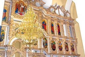 Großer goldener Kronleuchter in einer Kirche, vor dem verzierten Wandbild mit christlichen Figuren
