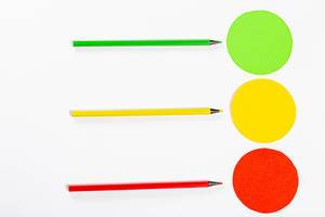 Grüne, gelbe und rote Stifte zeigen auf gleichfarbige Kreise in Form einer umgedrehten Ampel