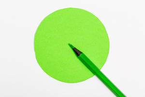 Grüner Holzmalstift zeigt in einen grünen Kreismittelpunkt als Symbol für richtige Entscheidungen