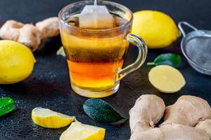 Grüner Tee mit Ingwer und Zitrone - Eine Tasse mit Teebeutel auf schwarzem Hintergrund