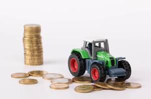 Grüner Traktor mit Münzen vor weißem Hintergrund