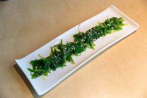 Grüner veganer Seealgensalat "Goma Wakame" mit Sesamkernen, im japanischen Restaurant, auf einem hellen Holztisch
