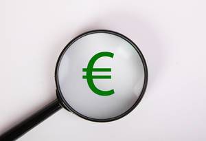 Grünes Euro-Zeichen, vergrößert dargestellt unter einer Lupe