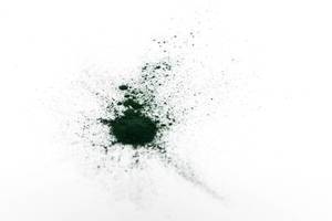 Grünes Spirulina-Pulver liegt verteilt auf einer weißen Fläche