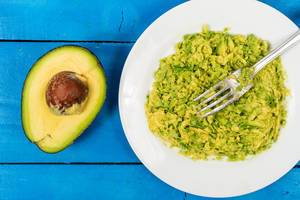 Guacamole: Zerdrückte Avocado liegt mit einer Gabel auf einem Teller