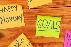 Guter Start in die Woche: Bunte Haftnotizzettel mit dem Text "Goals" - Ziele und "Happy Monday" - Fröhlichen Montag - kleben auf auf einem Holzbrett