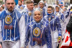 Guys and girls in traditional blue and white costumes belonging to the dance corps of the Kölner Rheinveilchen parade wearing a rain poncho on rainy Rose Monday 2020 in Cologne