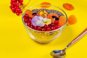 Haferflocken mit Früchten, Chiasamen und essbaren Blumen in einer kleinen Glasschüssel mit Löffel